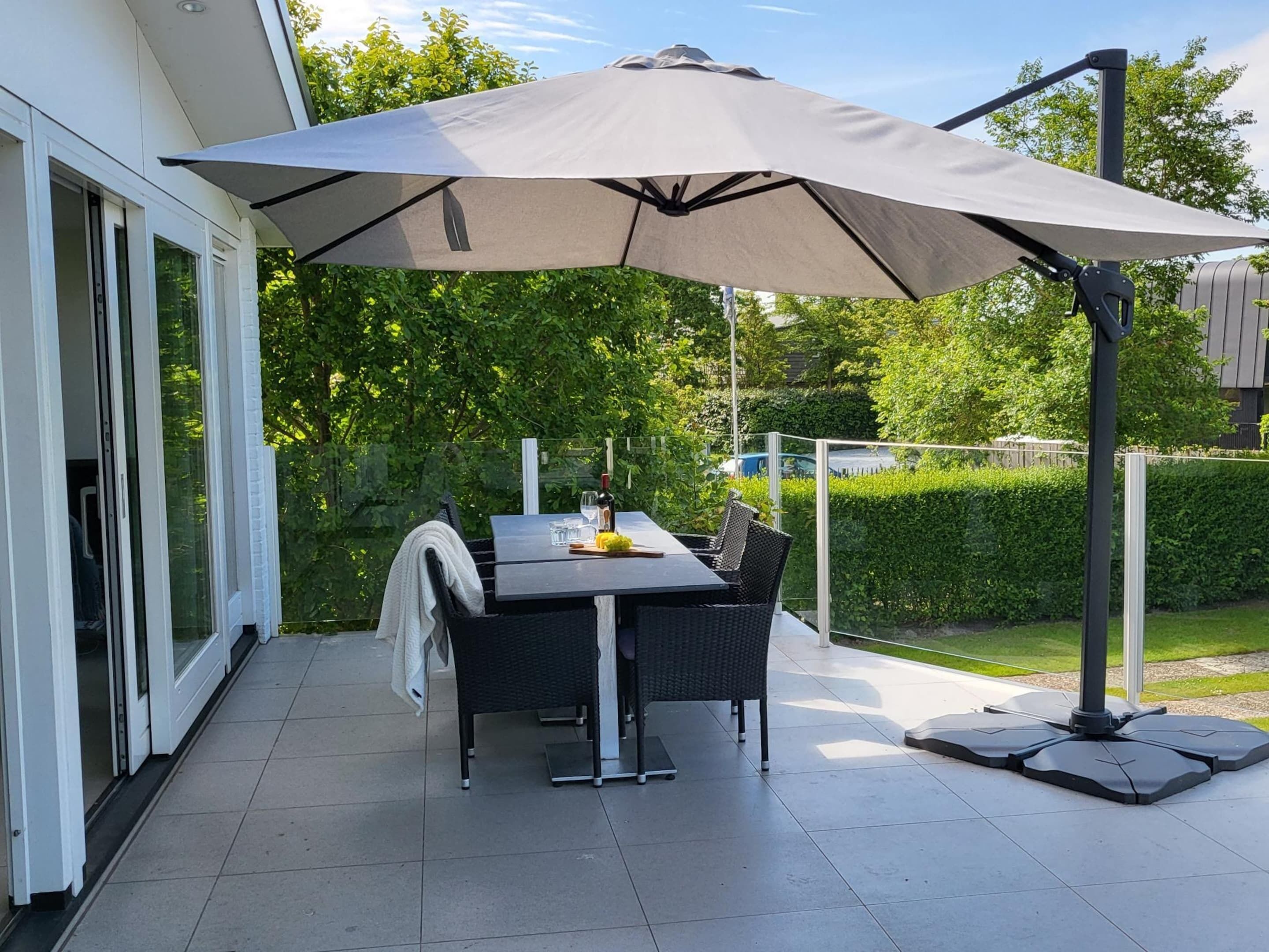 An outdoor patio with a table and chairs, a large umbrella, and a glass door leading to a covered area.