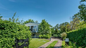 A modern house with a paved pathway leading to the entrance, surrounded by lush greenery and trees. - Holiday Home Zeeland Near Veerse Meer (Kamperland)