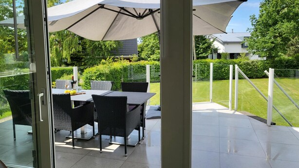 A patio with a table and chairs, a large umbrella, and a glass door leading to a garden. - Holiday Home Zeeland Near Veerse Meer (Kamperland)