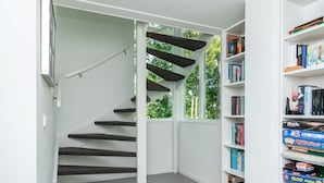 A staircase with dark steps leading to a landing, surrounded by white walls and a bookshelf filled with board games. - Holiday Home Zeeland Near Veerse Meer (Kamperland)