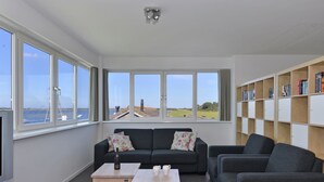 Ein modernes Wohnzimmer mit einem großen Fenster, einer Couch, zwei Beistelltischen und einem Bücherregal.