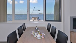 Ein Essbereich mit großem Tisch, sechs Stühlen und Blick auf ein Gewässer mit einem Kran.