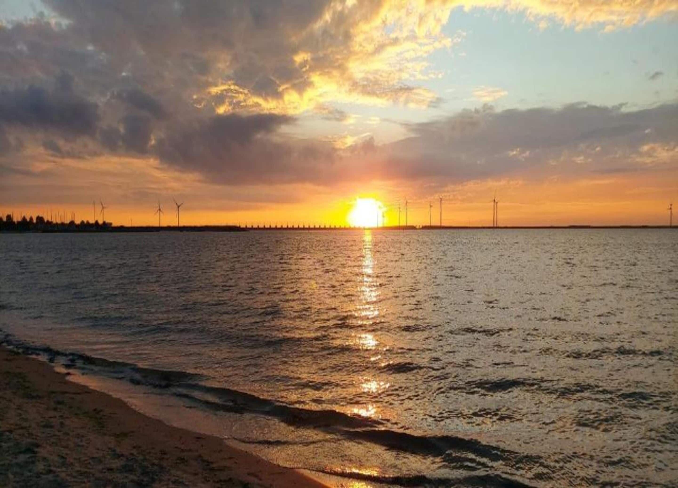 A sunset over a body of water with wind turbines in the distance.