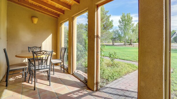 A patio with a table and chairs, large windows, and a view of a grassy area.