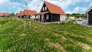 Uma fileira de casas modernas com telhados vermelhos, um campo gramado com flores brancas e um céu azul límpido.