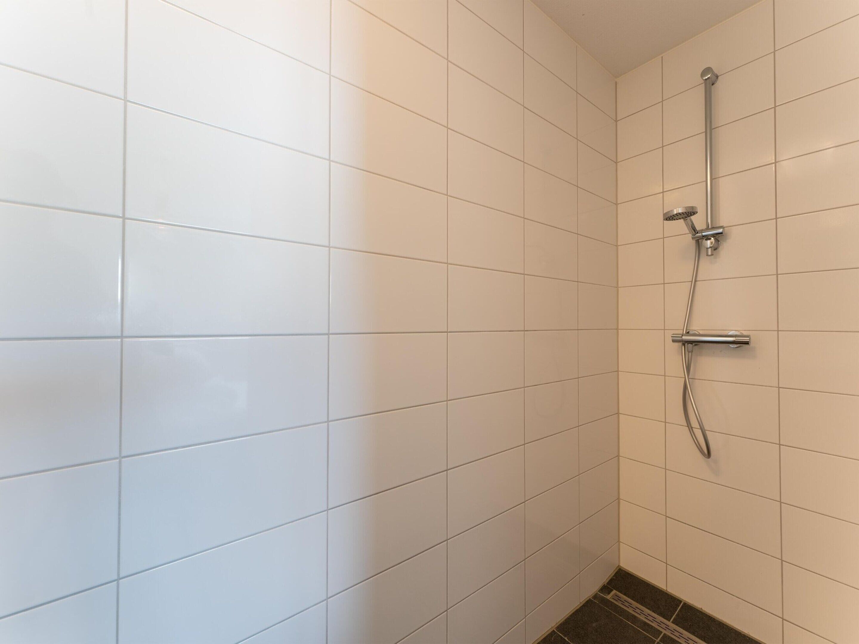 A bathroom with white tiled walls and a shower area.