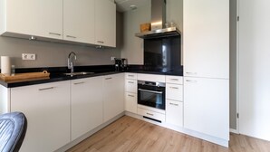 Uma cozinha moderna com armários brancos, bancada preta, exaustor de aço inoxidável e forno embutido.