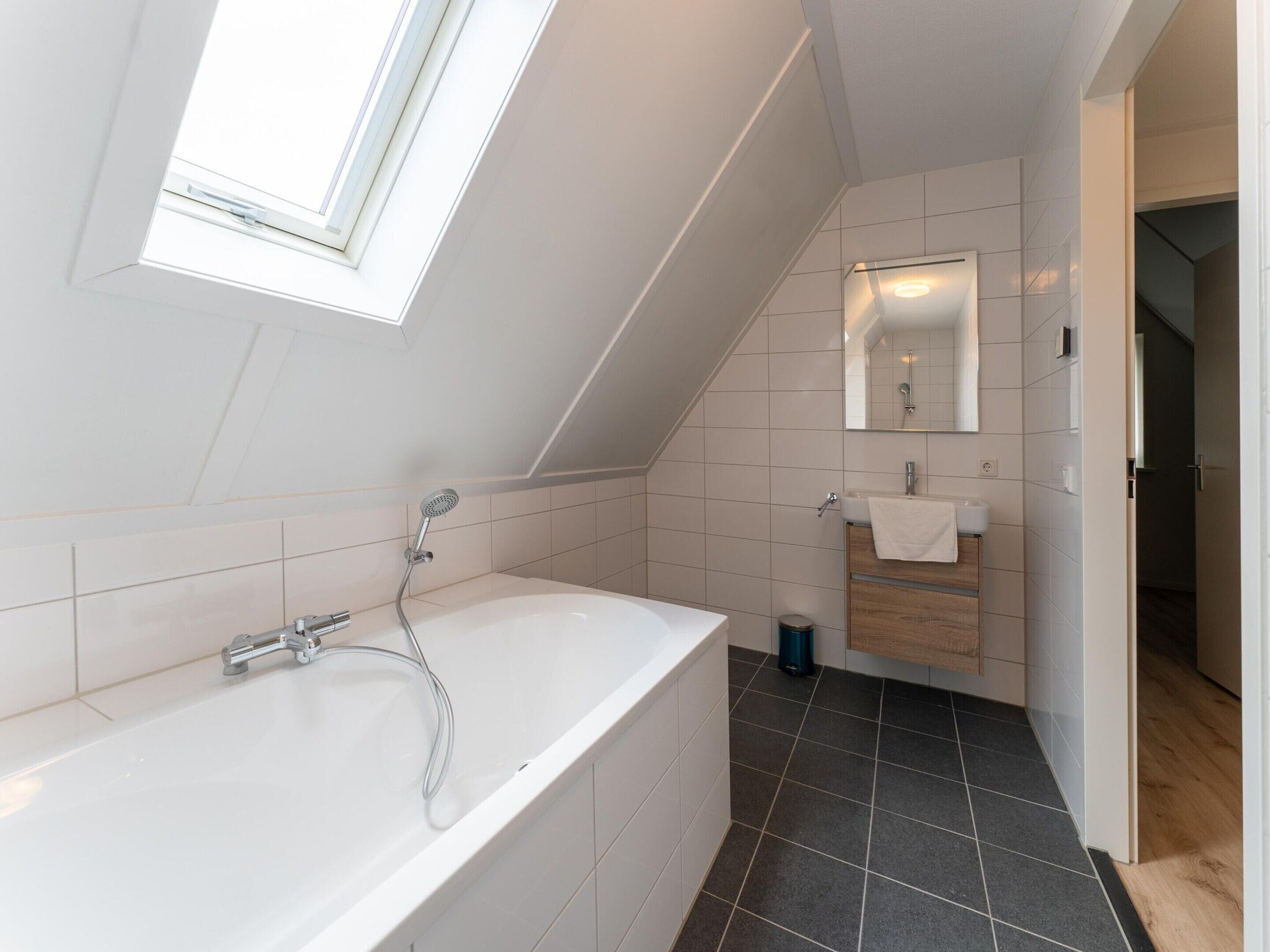 Ein modernes Badezimmer mit einer freistehenden Badewanne, einer Dusche, einem Waschtisch mit Spiegel und einem Fenster.