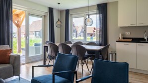 Uma sala de estar moderna com sofá, mesa de jantar com cadeiras, cozinha com armários e janelas amplas com cortinas.