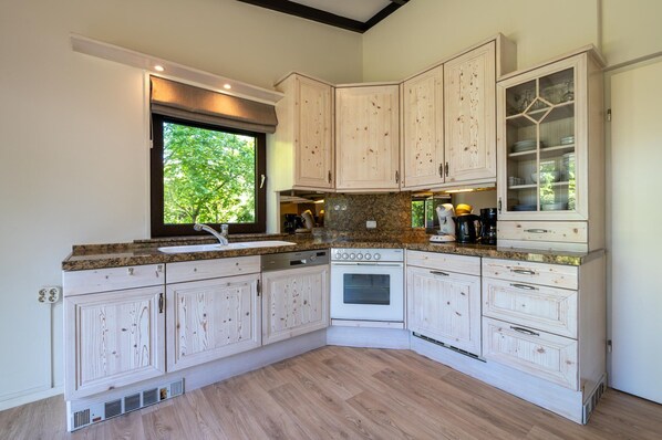 A kitchen with white cabinetry, a granite countertop, a built-in oven, and a window with a view of greenery. - Bungalow Near Lake Veere With Sunny Terrace (Kamperland)