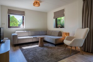 A modern living room with a sectional sofa, a round coffee table, a white armchair, and a TV on a wooden stand. - Bungalow Near Lake Veere With Sunny Terrace (Kamperland)