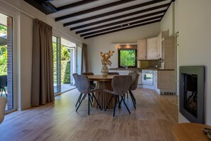 A modern kitchen with wooden cabinets, a dining area with a round table and chairs, and a fireplace. - Bungalow Near Lake Veere With Sunny Terrace (Kamperland)