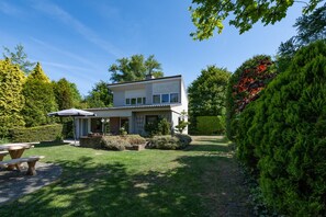 A two-story house with a patio area, a small garden, and a well-maintained lawn. - Bungalow Near Lake Veere With Sunny Terrace (Kamperland)