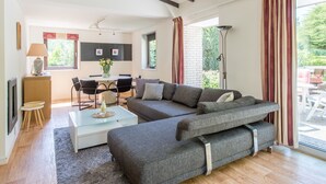 En moderne stue med en modulsofa, et spisebord med stole, et sofabord og et stort vindue med gardiner.