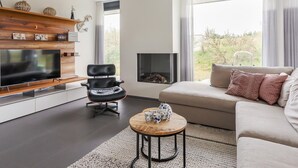 A modern living room with a flat-screen TV, a black leather chair, a beige sofa, and a fireplace. - Seaside Getaway With a Beautiful Garden (Kamperland)