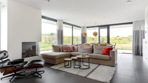 A modern living room with a sectional sofa, a black leather chair, a small coffee table, and a fireplace. - Seaside Getaway With a Beautiful Garden (Kamperland)