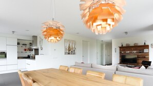 A modern living space with a wooden dining table, leather chairs, a sofa, and a TV mounted on a wooden wall. - Seaside Getaway With a Beautiful Garden (Kamperland)