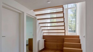 A modern staircase with wooden steps and a glass railing, leading to a room with a wooden floor and a window overlooking greenery. - Villa Sternlaan 24 Kamperland (Kamperland)