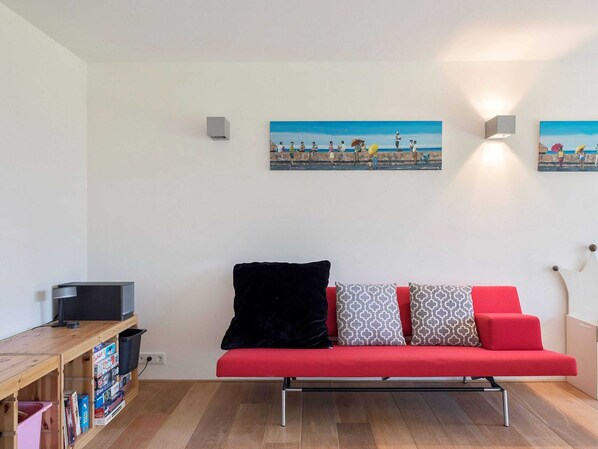 Una sala de estar moderna con un sofá rojo, un televisor sobre una estantería de madera y dos cuadros colgados en la pared.
