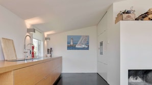 A modern kitchen with a wooden countertop, stainless steel sink, and a painting of a lighthouse. - Villa Sternlaan 24 Kamperland (Kamperland)