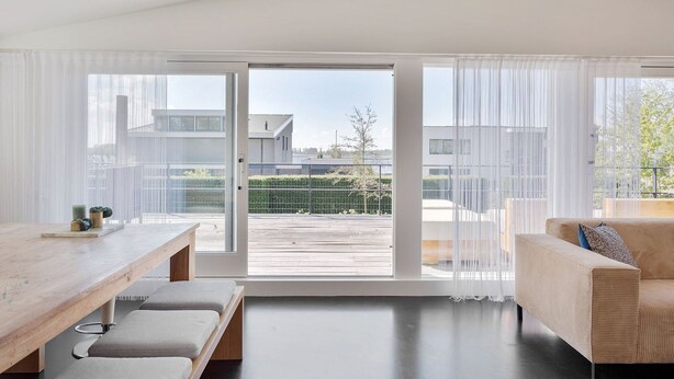 A modern living room with a wooden dining table, a sofa, and a large sliding glass door leading to a balcony. - Villa Sternlaan 24 Kamperland (Kamperland)