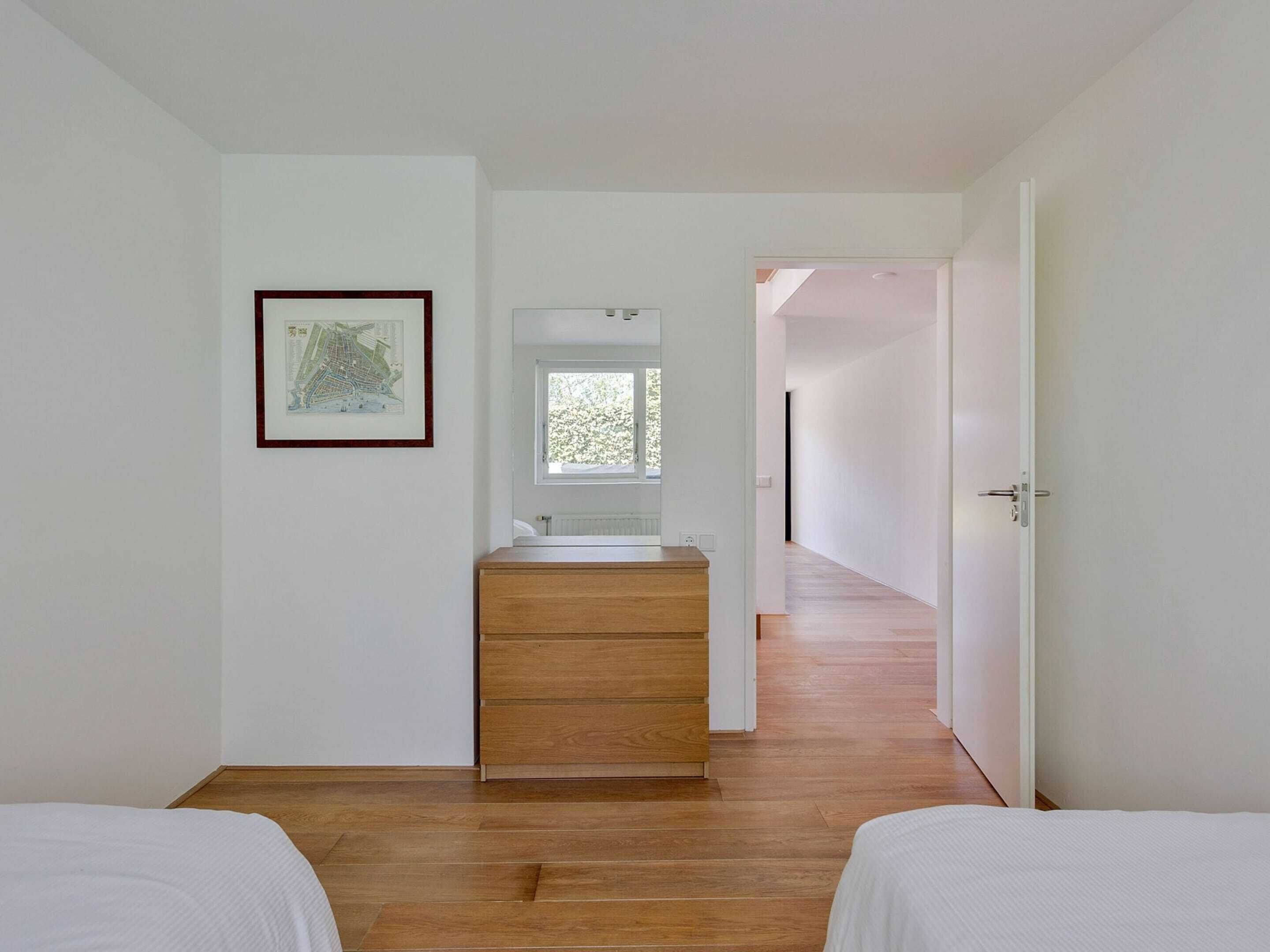 Une chambre avec deux lits, une commode en bois, une carte encadrée et une fenêtre.