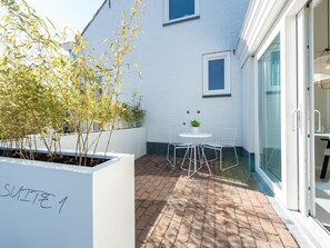 A small patio with a white table and chairs, a potted plant, and a white planter labeled "SUITE 1". - Holiday Home Near Beach in Zeeland (Oostkapelle)