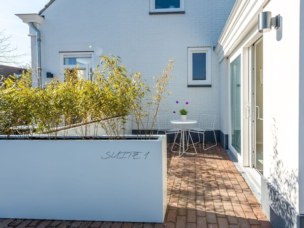 A modern outdoor patio with a white wall, a small round table, and two chairs. - Holiday Home Near Beach in Zeeland (Oostkapelle)