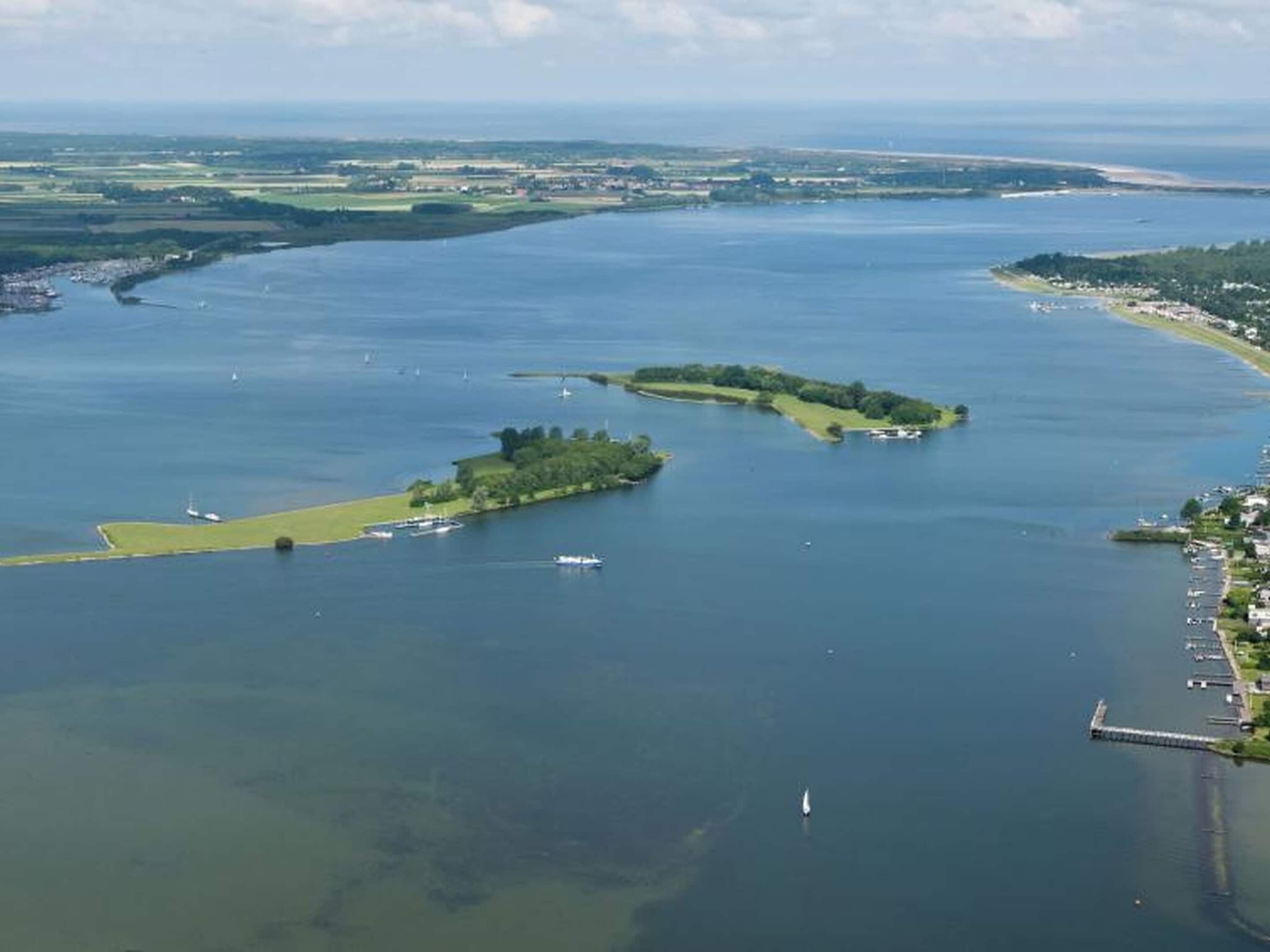 Eine Luftaufnahme einer Küstenlandschaft mit zwei kleinen Inseln, einem Yachthafen mit Booten und einem Steg.