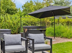 An outdoor seating area with two chairs and a large umbrella, surrounded by lush greenery and a wooden deck. - Apartment Near North Sea Beach (Kamperland)