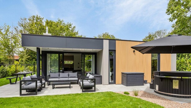 Een modern huis met een terras, meubilair buiten en een jacuzzi.