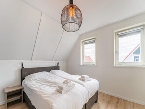 A bedroom with a bed, two windows, a hanging light fixture, and a wooden nightstand. - Beach Bliss Romantic Retreat (Scherpenisse)