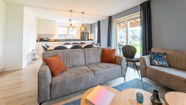 A modern living room with a grey sofa, a wooden coffee table, and a dining area with a kitchen in the background. - Beach Bliss Romantic Retreat (Scherpenisse)