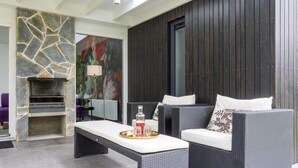 A modern outdoor seating area with a stone fireplace, wicker furniture, and a dark wooden backdrop. - Holiday Home Near Veerse Meer (Kamperland)