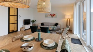 A modern living room with a dining area, featuring a large window, wicker ceiling lamps, and a flat-screen TV. - Apartment Kamperland Near Veerse Meer (Kamperland)