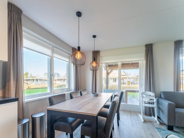 A modern dining area with a wooden table and chairs, large windows with curtains, and a view of the outside.