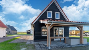 Une maison moderne avec une façade sombre, un toit rouge et une terrasse couverte.