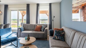 A modern living room with a sofa, armchairs, and a coffee table. Large windows offer a view of the outdoors.