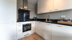 A modern kitchen with white cabinets, a black countertop, stainless steel appliances, and a wooden floor.