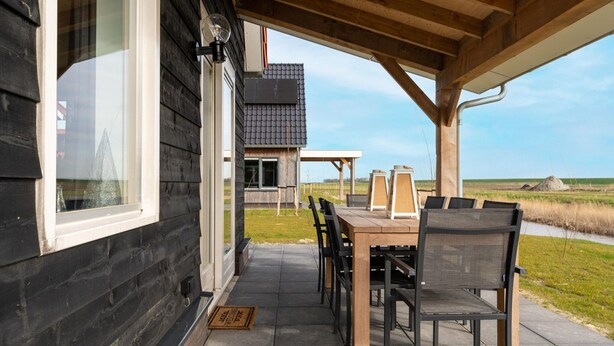 A wooden house with a covered patio, a dining table with chairs, and a view of the landscape.