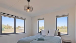 A bedroom with a large bed, two windows, a hanging light fixture, and a small bedside table.
