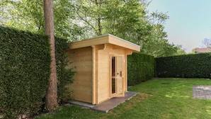 Un petit abri en bois, situé dans un jardin bien entretenu, avec une haie et un arbre à proximité.