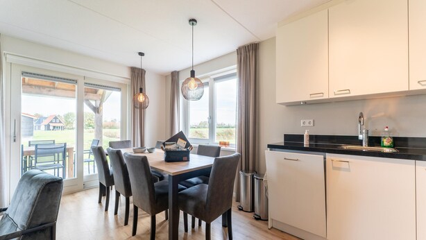 Una cocina moderna con armarios blancos, encimera negra y un comedor con mesa y sillas de madera.