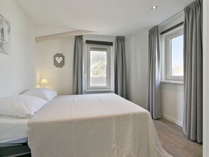 A bedroom with a bed, a window with curtains, a bedside lamp, and a heart-shaped decoration on the wall. - Holiday Home Near Sophia Beach and Marina (Kamperland)