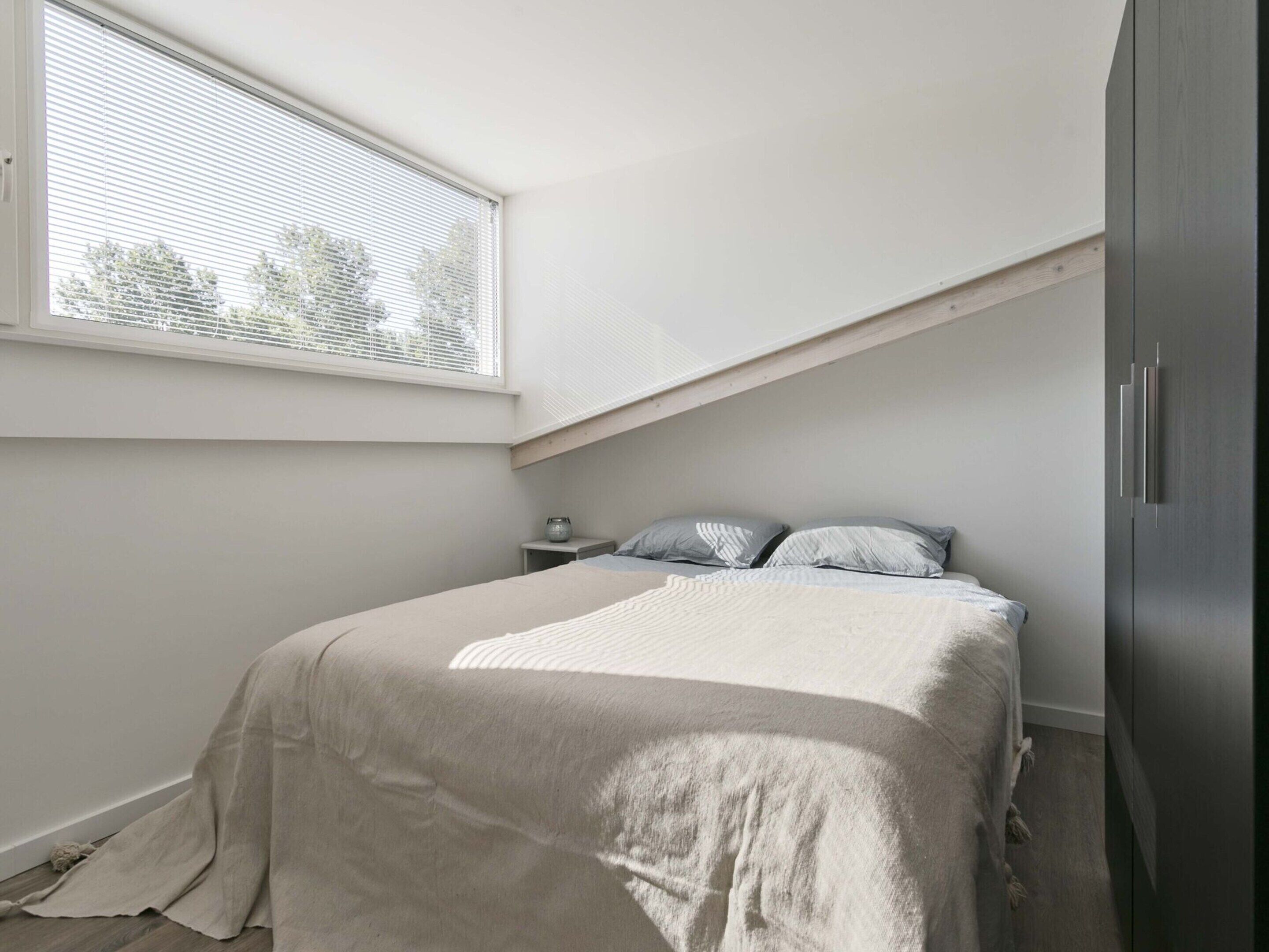 A bedroom with a bed, a nightstand, a window, and a wardrobe.