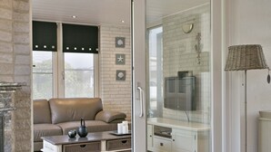 A modern living room with a leather sofa, a glass door leading to a kitchen area, and a television mounted on the wall.