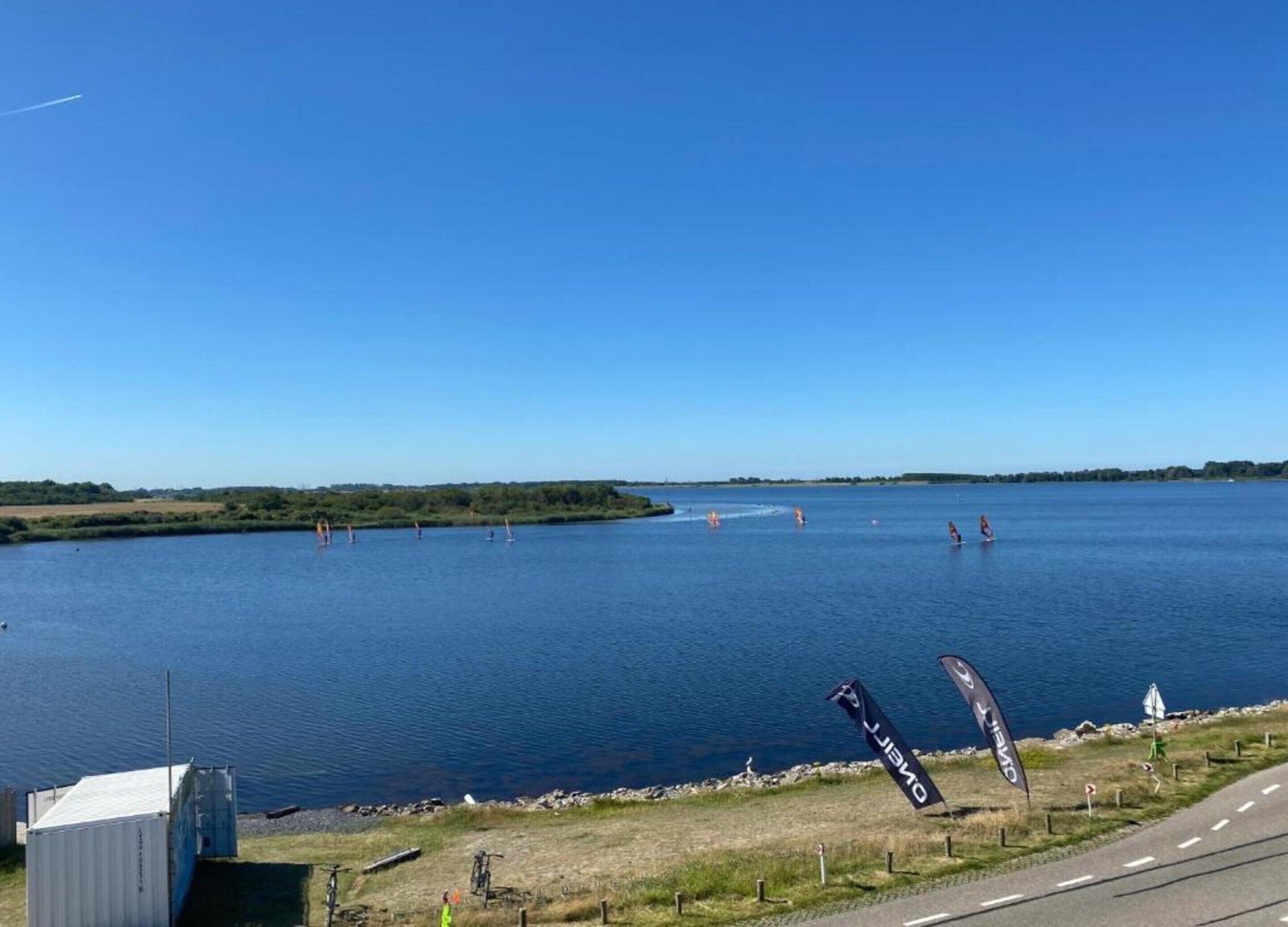 A large body of water with sailboats, a road, and a small building near the shore.