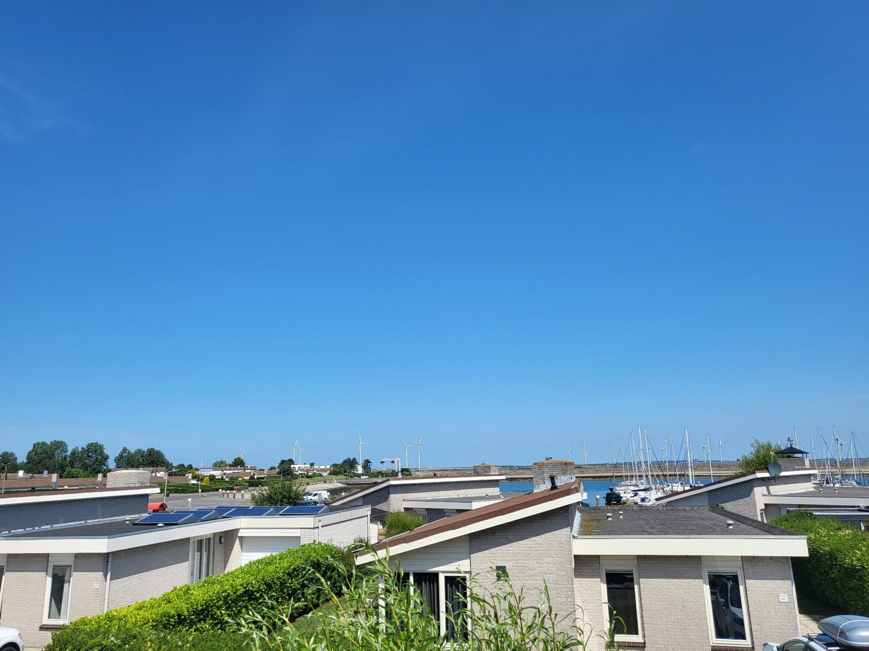 A coastal residential area with modern houses, some with solar panels, and a marina in the background.