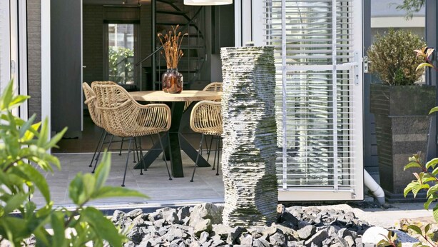 An outdoor dining area with wicker chairs, a table, and a vase of dried flowers.