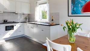 A modern kitchen with white cabinets, a built-in oven, and a window. There is a dining table with chairs and a vase of flowers. - House Near Veerse Meer and North Sea Beach (Kamperland)